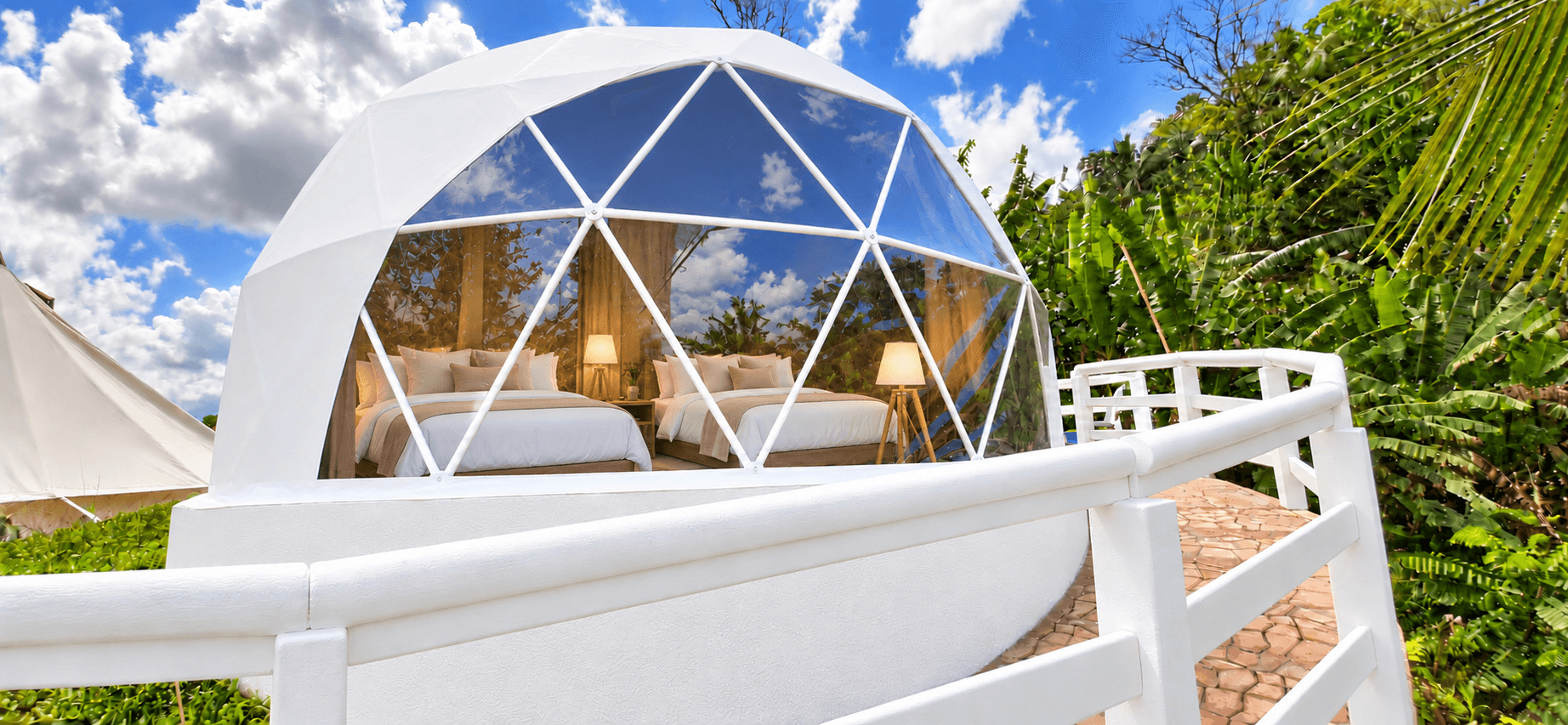 Deluxe Dome exterior, a white glamping dome with a glass front surrounded by greenery
