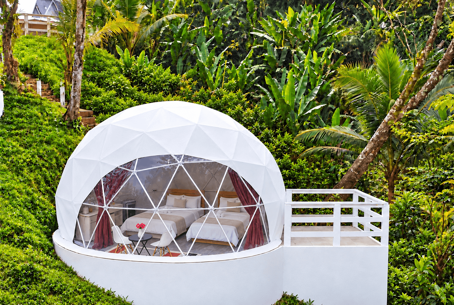 Family Dome exterior, a white glamping dome with a glass front and a deck on a green hillside